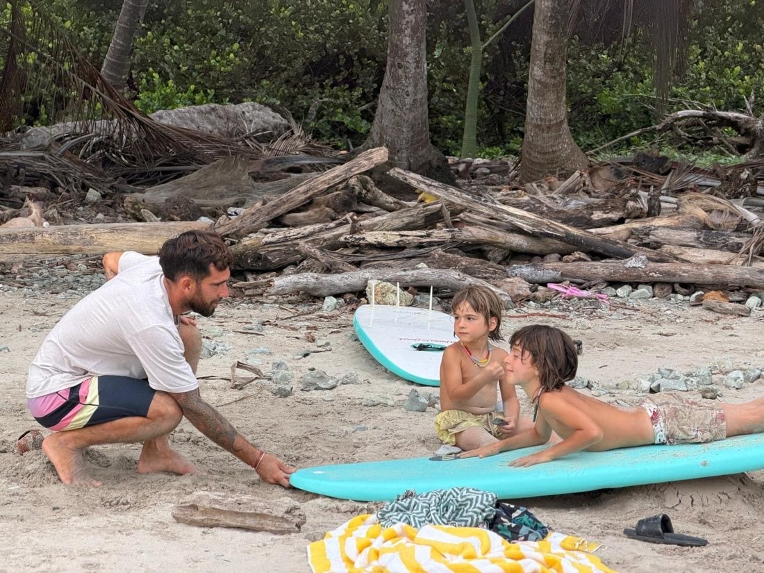 A coach teaching two kids on the sand before they paddle out
